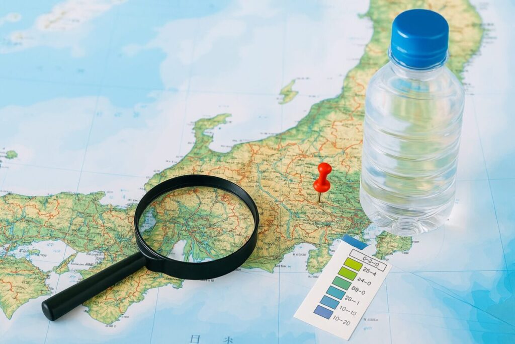 日本地図の上に置かれたペットボトルと採水地を示すピンとルーペ